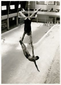 Shirley Wightman and Freddie Quadros hanging from the trapeze high above the pool, 1941